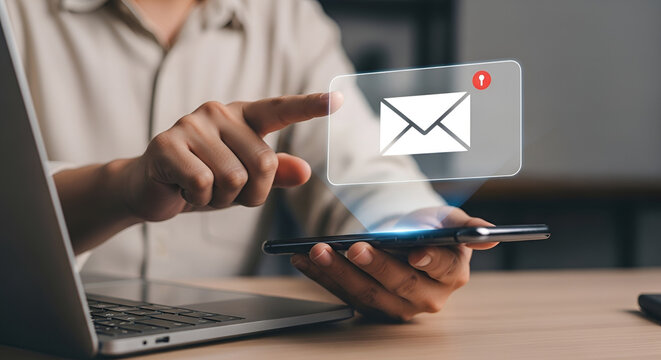 Email Notification on Smartphone A person's hand touches a smartphone screen displaying a holographic email icon signifying a new message notification with a laptop in the background