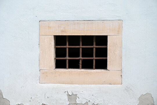 Basement or cellar window fitted with a dark metal security grille, serving as a symbol of captivity and imprisonment. A barred cellar window.