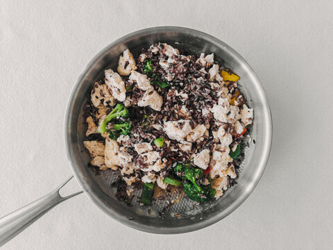 Nutritious chicken and vegetable stir-fry with black rice in a stainless steel cooking pan.