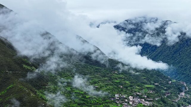 Aerial view of a mountain village surrounded by lush green terraces shrouded in thick mist at Mount Siguniang, Aba Prefecture, Sichuan, China.