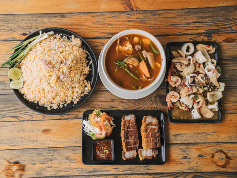 Authentic Thai Food Spread with Fried Rice, Spicy Seafood, Soup, and Crispy Pork Belly.