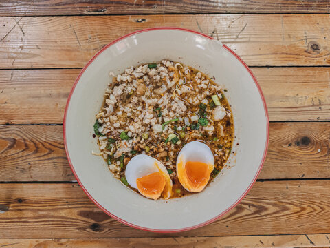 Delicious Thai spicy noodle soup with minced pork and soft-boiled eggs on a wooden table.