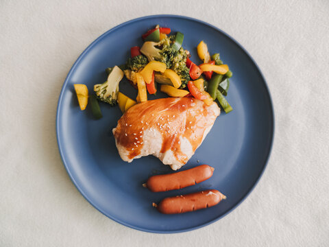 Healthy Chicken Breast Meal with Colorful Stir-fried Vegetables and Sausages on a Blue Plate