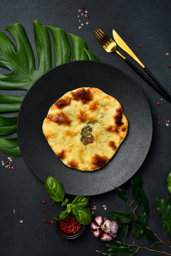 Freshly baked meat flatbread served on round dark plate. Traditional Georgian kubdari khachapuri pie placed on table. Tasty homemade pastry surrounded by spices and chili.