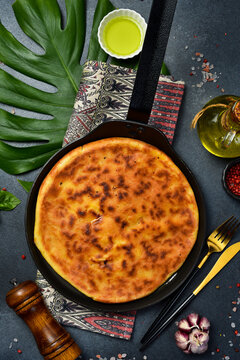 Traditional roasted round pie baked inside black frying pan top view. Tasty golden cheese flatbread surrounded by garlic and chili peppers. Gourmet homemade meal recipe.