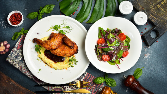Roasted golden half chicken served over smooth mashed potatoes with savory sauce. Fresh vegetable salad with cherry tomatoes placed beside toasted bread basket. Delicious dinner.