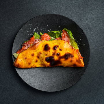 Tasty Italian folded pizza stuffed with smoked salmon. Fresh lettuce leaves and ripe tomatoes fill the baked dough. Delicious gourmet lunch served on dark dish.