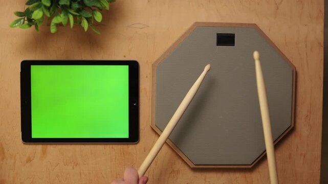 Drumsticks poised over tablet and practice pad, ready for action
