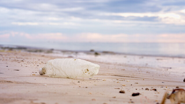 single-use plastic water bottle on a beach, ocean pollution, polluted nature and environment, indonesia, southeast asia