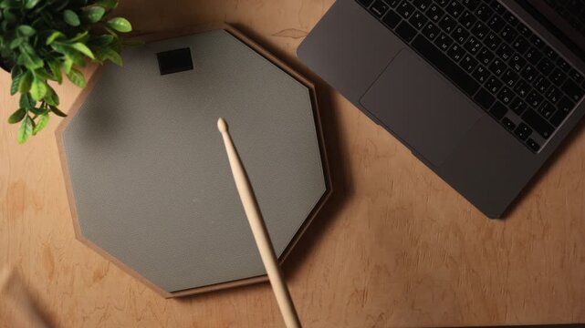 Overhead view of a laptop and drum practice pad on a wooden desk