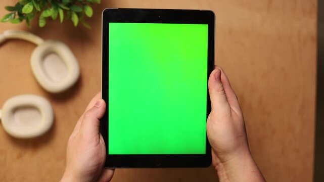 Person holding a tablet with a green screen and headphones nearby
