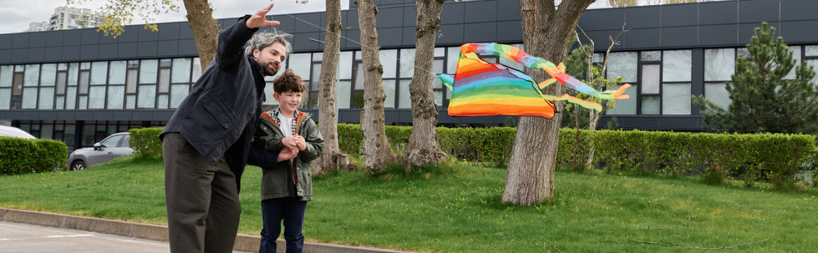 A joyful father and his son have fun flying a colorful kite outdoors.