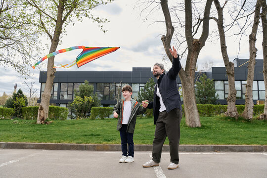 A joyful father and son are happily flying a colorful kite in nature.