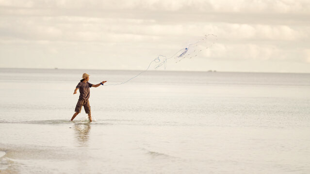 Indonesian fisherman throwing fishing net in sea or ocean to catch fish close to beach, indonesia, southeast asia, asian people