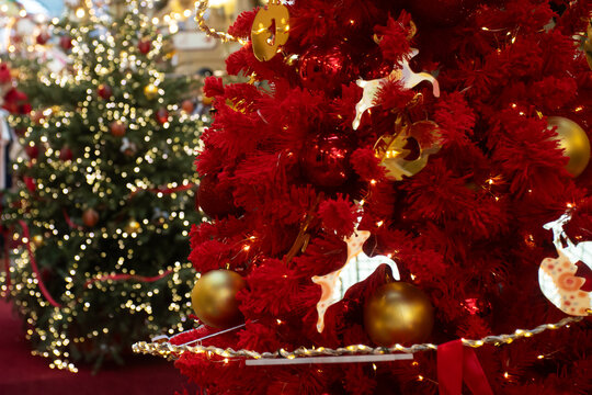 decorative red holiday tree installation with golden baubles and lit reindeer figures,framed with rope lights and ribbon,inside a shopping center with soft bokeh and seasonal ambience