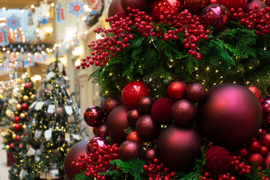 lush evergreen branches covered with red berry sprays and mixed baubles, lit by tiny warm lights, set in a busy indoor shopping center with soft seasonal festive bokeh