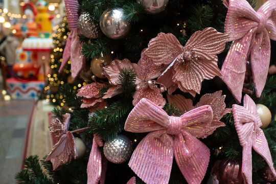 festive christmas tree dressed with large pink ribbon bows and sparkling poinsettia flowers, silver baubles and warm fairy lights, with blurred nutcracker display in background