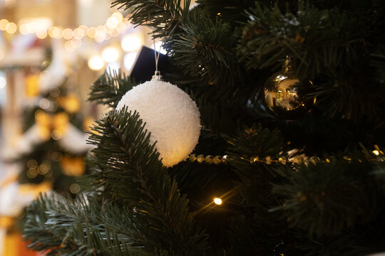 soft white fuzzy bauble and shiny gold ornament on a dark green christmas tree, warm twinkle lights and blurred festive background, elegant seasonal decoration and cozy mood