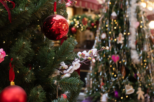 decorated christmas tree with red glossy baubles and a white blossom branch, festive indoor market background with multiple trees and bokeh lights, seasonal shopping atmosphere