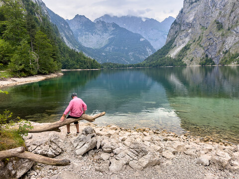 Elderly Man Taking a Break On an old old tree branch in the Bavarian Alps with mountain lake	
