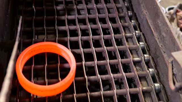 Industrial steel ring conveyor system showing hot glowing components cooling while moving along a transport line and accumulating into stacked storage piles inside a factory
