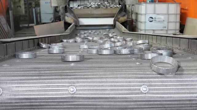 Industrial metal grinding and finishing process showing precision conveyor systems, automated belt polishing machinery, and water coolant treatments operating inside a modern manufacturing workshop pl
