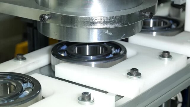 Industrial manufacturing machinery sorts, transports, and presses metallic ball bearings using blue conveyor belts and automated pneumatic systems in a factory plant