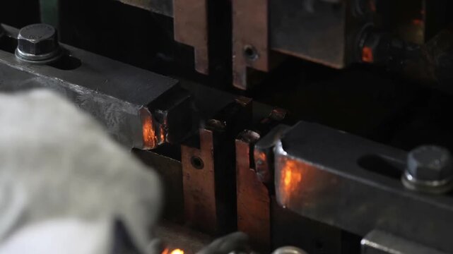 Factory worker operating heavy industrial machinery to weld metal chain links together during manufacturing production operations in a workshop