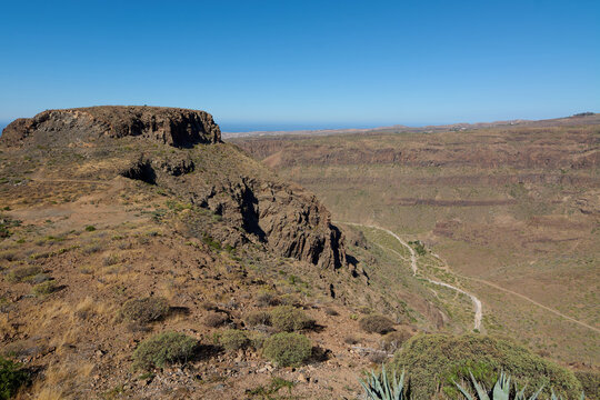 Majestic high-angle landscape view of the rugged volcanic cliffs and deep ravine of Degollada las Yeguas under a clear blue sky in Gran Canaria.