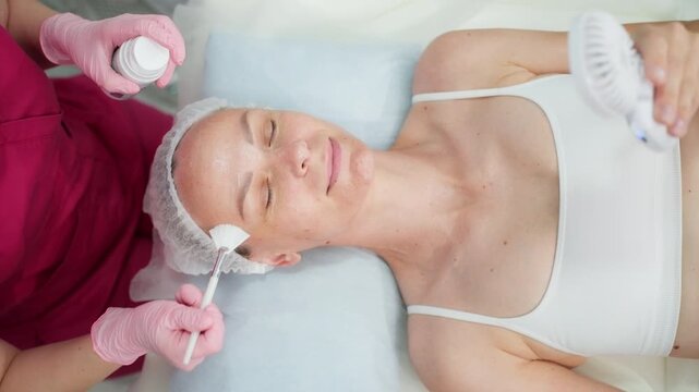 Female client receiving a relaxing facial skincare treatment while cooling her face with a handheld fan. Beauty wellness, stress relief, relaxation, skin care and peaceful self-care experience 