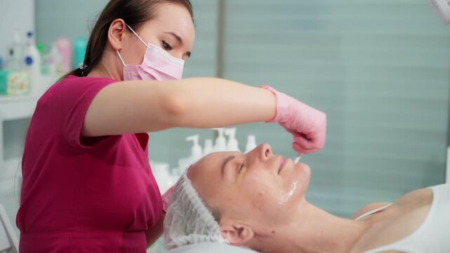 Professional esthetician performing a facial massage treatment, applying a nourishing cream mask to a woman's face in a beauty salon for skin rejuvenation and anti-aging care