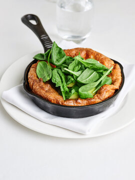 Dutch baby pancake with avocado and baby spinach served in a cast iron skillet, brunch menu item, healthy eating concept