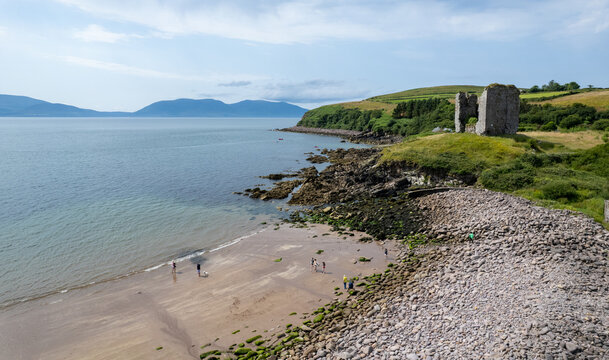 Drone aerial view of Minard castle ruin standing on a rocky beach with a coastal road. Ireland, irish landscape