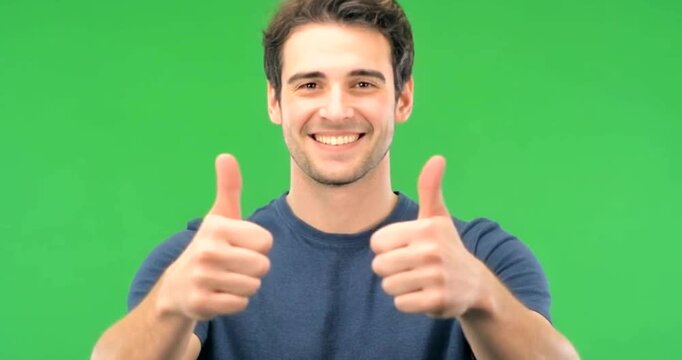 Young Man Giving Thumbs Up Gesture Smiling on Green Screen Background.
