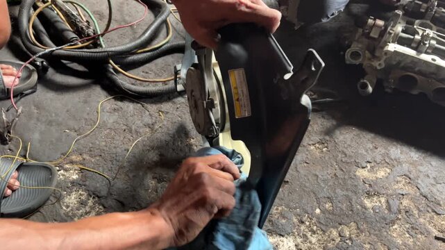 Mechanic cleaning a used car engine extra fan in salvage auto parts shop in Indonesia. The condition is quite dirty and dark