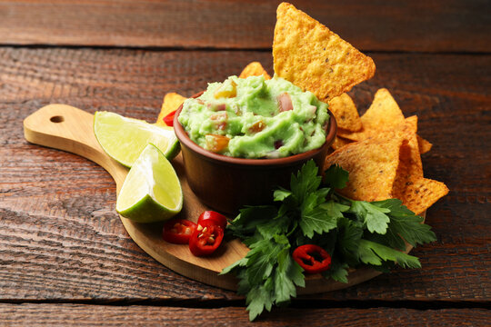 Delicious avocado dip with vegetables in bowl, tortilla chips and products on wooden table, closeup
