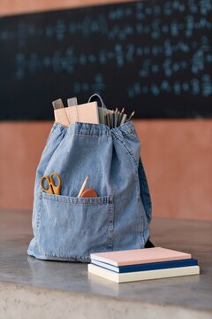 Denim drawstring backpack with pencils scissors and notebooks on desk for classroom background and study poster design