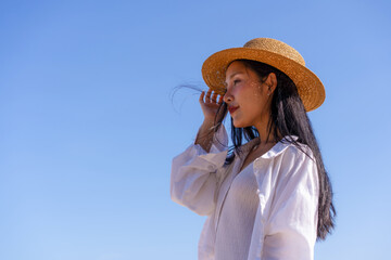 Side Profile Portrait of Young Woman Wearing Straw Hat Against Clear Blue Sky, Summer Vacation, Beach Travel, Relaxation, and Lifestyle © kwanchanok