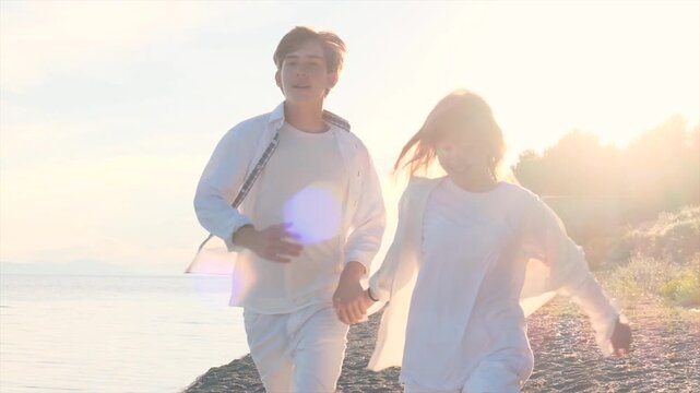 Happy teenage siblings running hand in hand on the beach at sunset, young brother and sister wearing white clothes, expressing joy and carefree happiness, enjoying time together in harmony