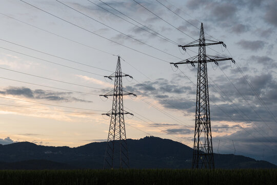 Power lines and towers are visible during sunset in a rural area with distant hills in the background. The sky has light clouds.