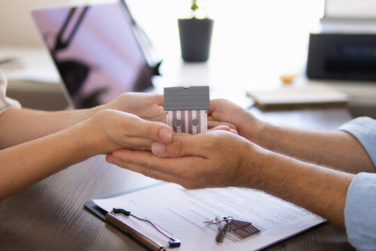 Hands of a real estate agent and a client are seen transferring a house model, representing the successful conclusion of a home purchase, property deal, or mortgage process