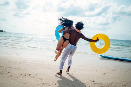 Friends, diverse couple having fun with colorful inflatable rings at the seaside