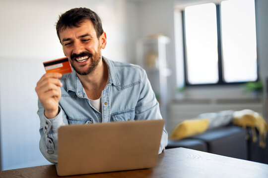 Smiling man working on an e-commerce business at home using laptop and credit card