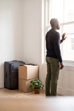 Man looking out the window while standing near unpacked boxes  