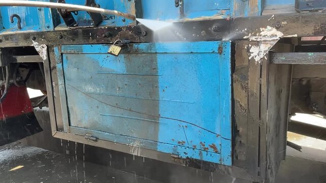 Pressure washing a blue truck body panel removes dirt and grime with a powerful water spray, showing vehicle cleaning in progress at an outdoor commercial washing area during truck washing.