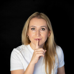 Naklejka premium portrait of a beautiful blonde woman smiling and showing sign hands for shut up. Isolated on black background with copy space and clipping path