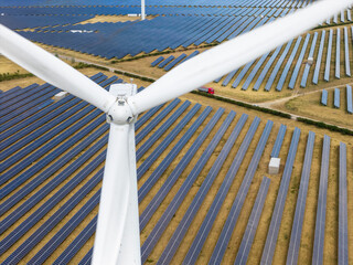 Wind Turbine Blades Looming Over a Vast Landscape Filled With Rows of Solar Panels © Tom