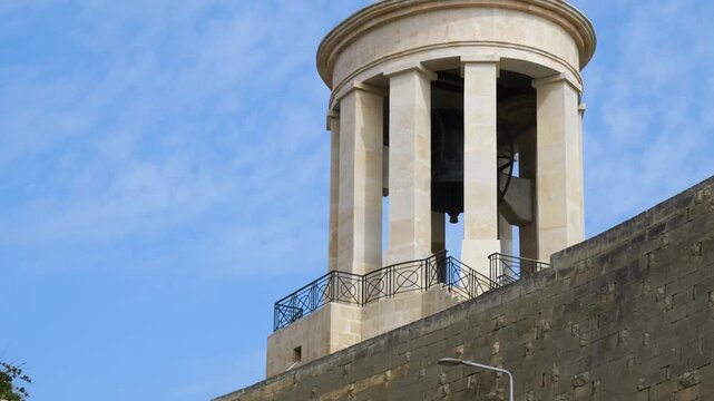 siege bell hangs beneath a columned rotunda dome close up view valletta memorial architecture against blue sky siege bell memorial malta war memorial world war two memorial valletta bastion