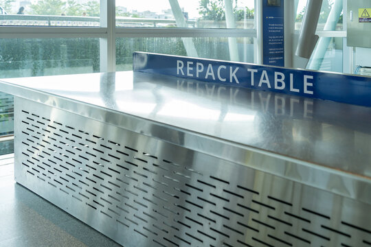 Modern airport repack table with a stainless steel surface and perforated metal panel, located  in an airport terminal.