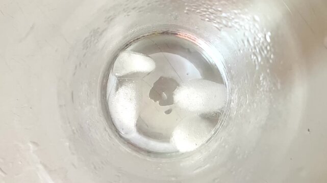 Fondo de vaso de cristal con agua y cubitos de hielo en movimiento, girando